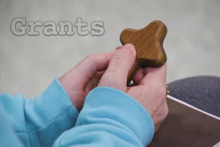 Close-up of hands with a person in a blue shirt holding a small wooden cross.